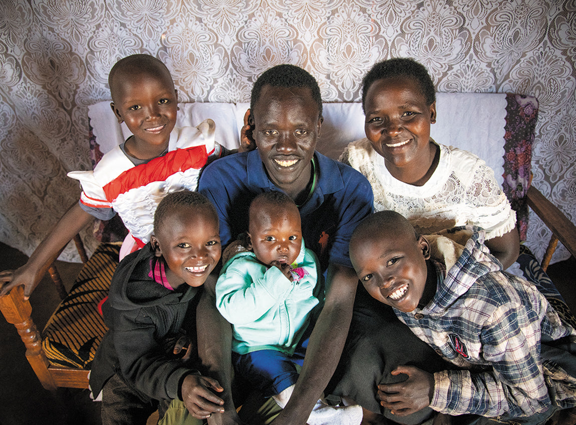A man, his wife and four children embrace on a couch, smiling.