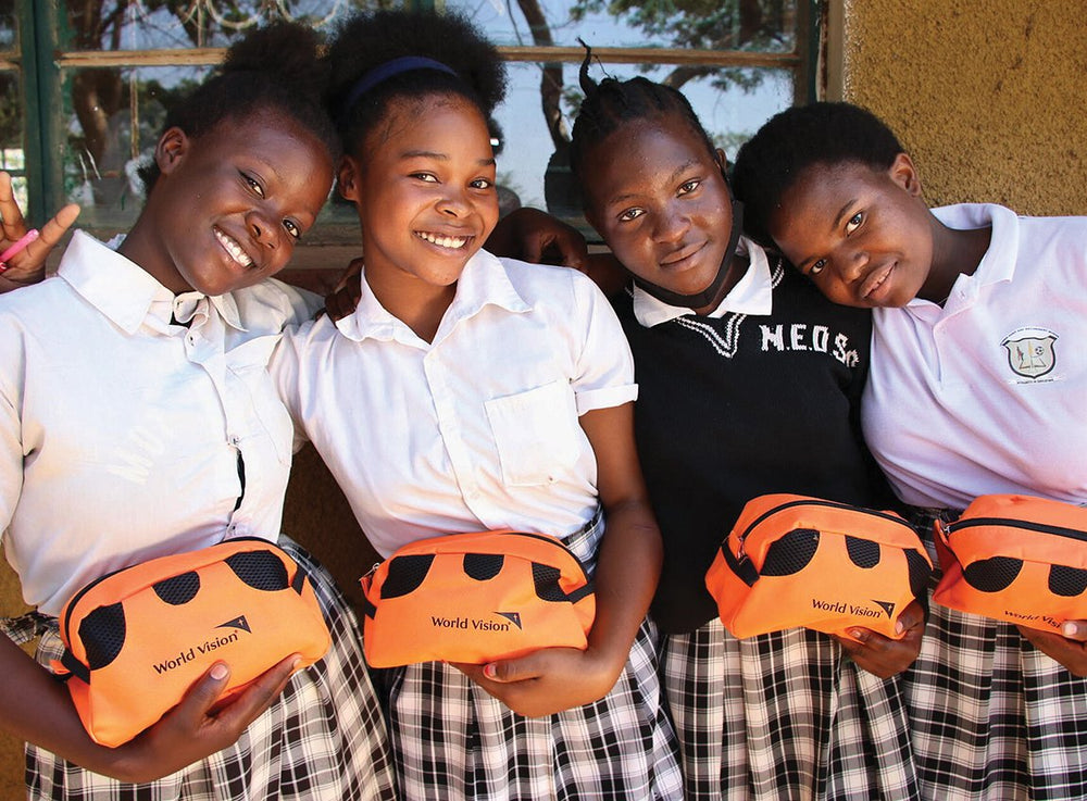Four young girls in uniforms with plaid skirts smile for the camera. Each of them hold a small travel pouch that serves as a hygiene kit.