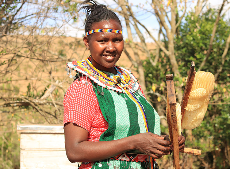 A woman smiles as she holds honeycombs from her recent honey harvest from her beehives.