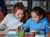 Two little girls sit side by side, coloring together.