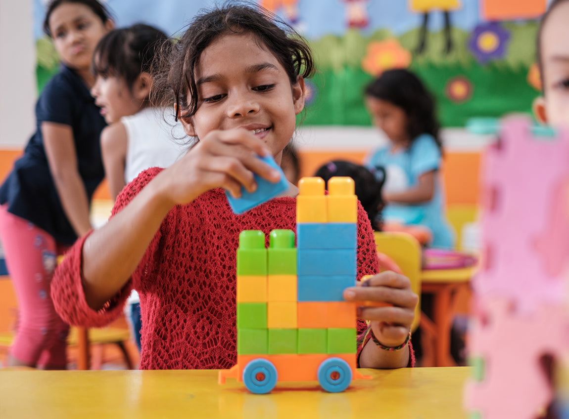 A young girl stacks colourful blocks in a classroom.