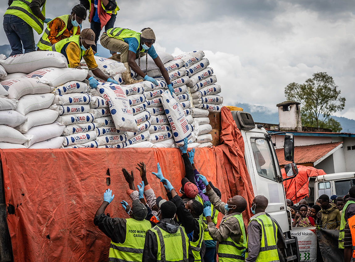 Volunteers stand on top of a truck, distributing large bags of emergency food to volunteers below.