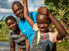 A smiling child dangles a fish from a string, while his parents stand behind him.