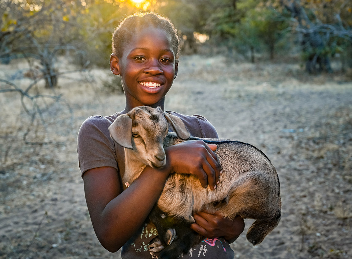 A smiling girl holds a goat in her arms outside.