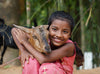 A smiling girl holds a goat in her arms outside.