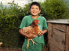 A smiling young boy wearing a green T-shirt holds a rooster in his arms.