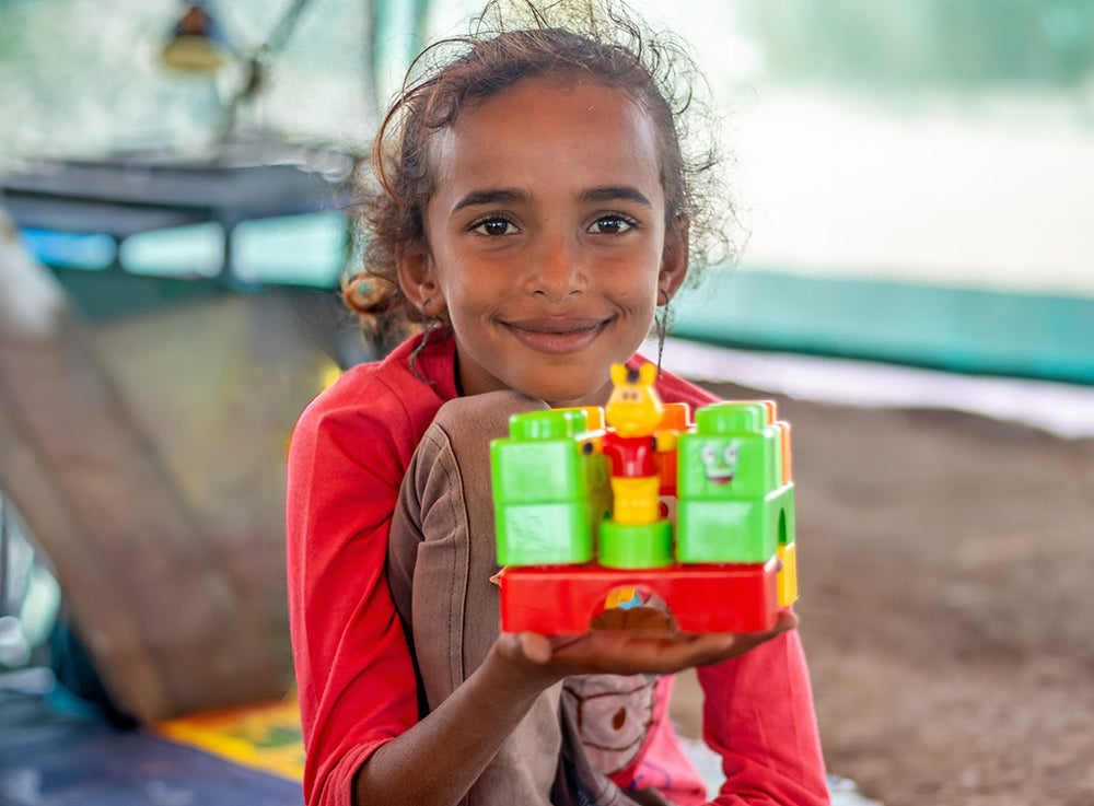 A girl smiles as she holds up an educational toy.  