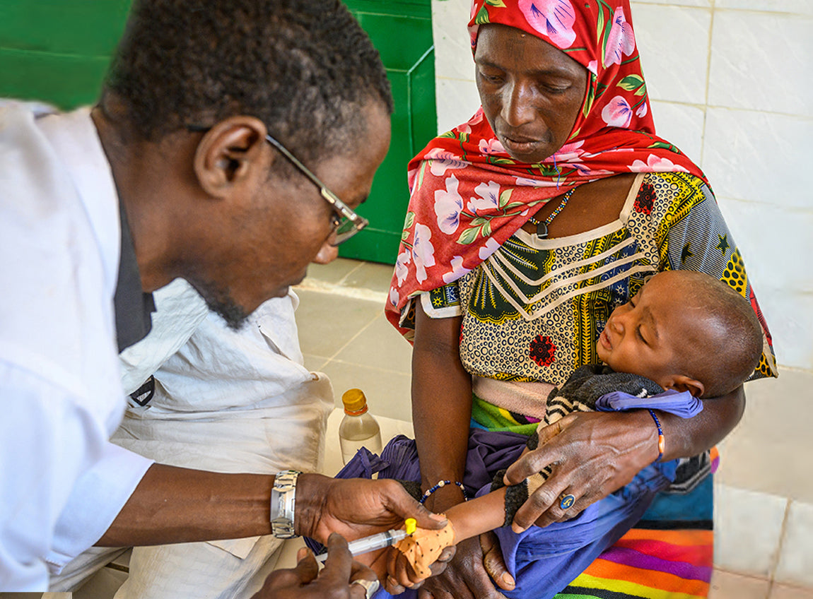 A woman holds her baby in her arms while he receives a vaccination from a doctor.
