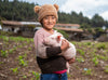 A young girl standing in a farmer’s field smiles as she holds a sleeping piglet in her arms.
