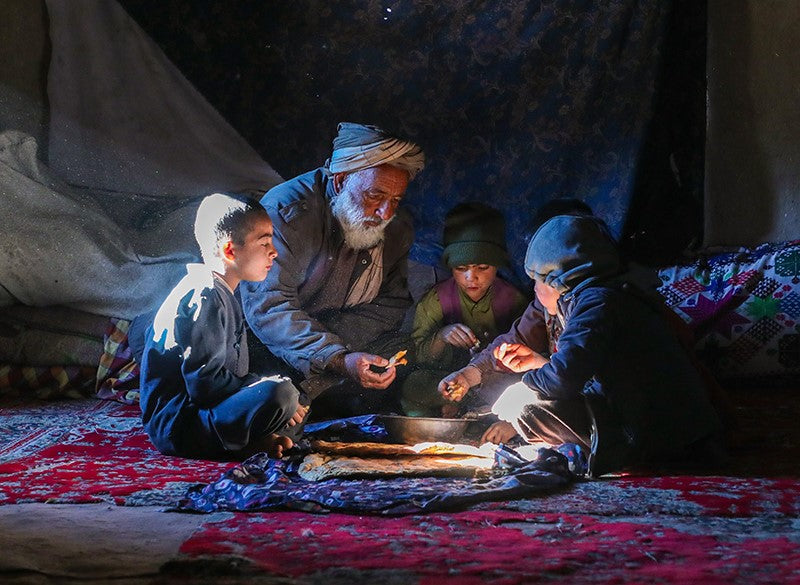 A father and his children gather round in a circle to eat food.