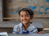 A little girl wearing school uniform smiles while sitting at her desk.