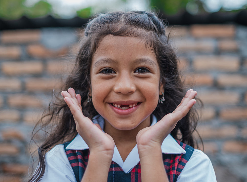 A girl smiles to the camera with her hands framing her face.