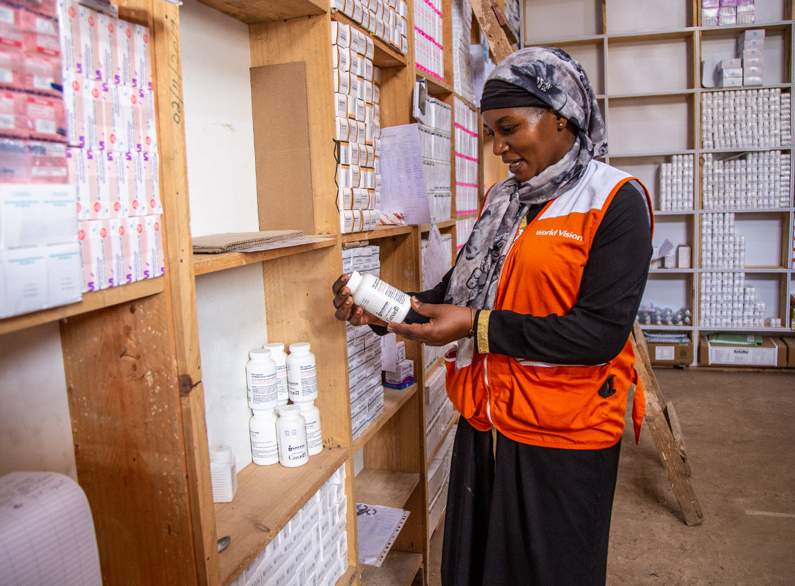 A volunteer stands inside a stocked pharmacy, reading the side of a pill bottle.