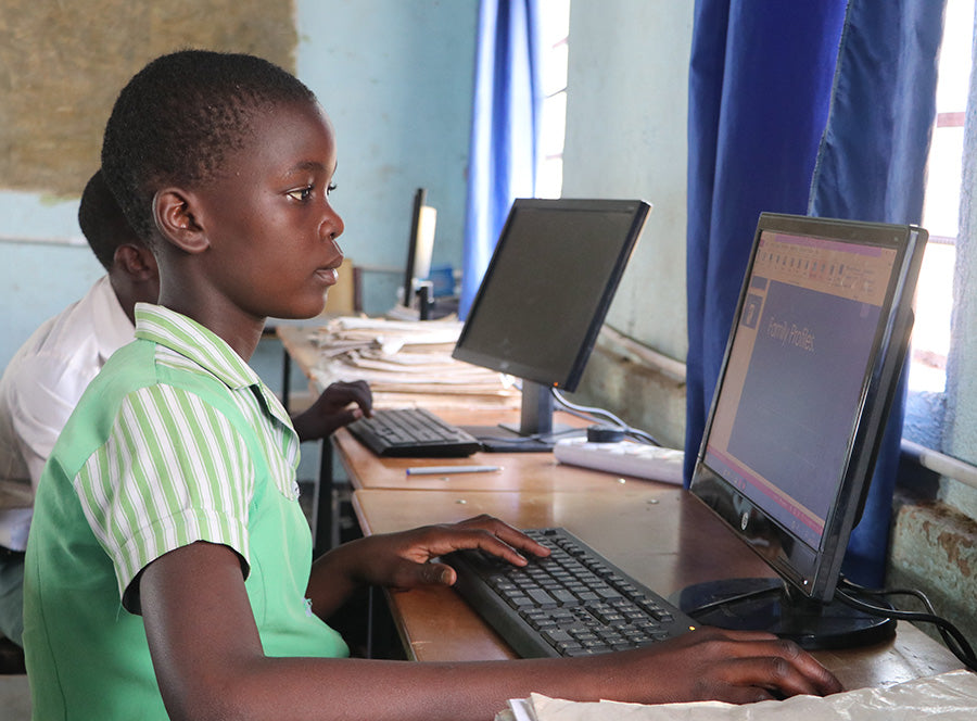 A girl sits at a desk while working on a  computer.