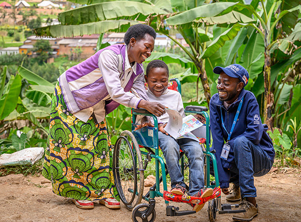 A woman and a man smiling and engaging with a child in a wheelchair outdoors.