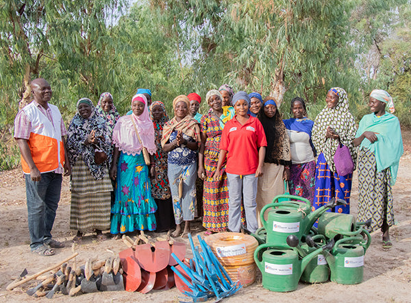 Members of a community smile as they stand behind tools provided by World Vision.