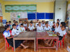 Children smile while sitting at their desks in a classroom.