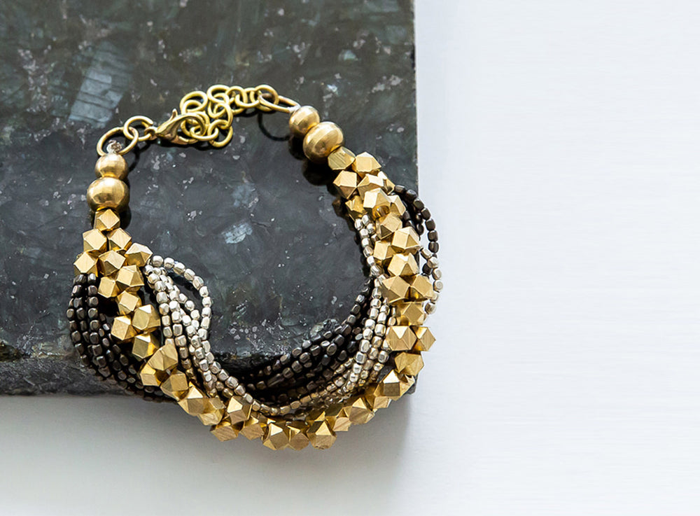 A multi-strand bracelet made of gold, black, and silver beads on top of a black stone.