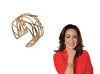 An adjustable cuff bracelet with twig designs in brass finish. On the right, a woman in a red blouse poses with the bracelet on her right arm.