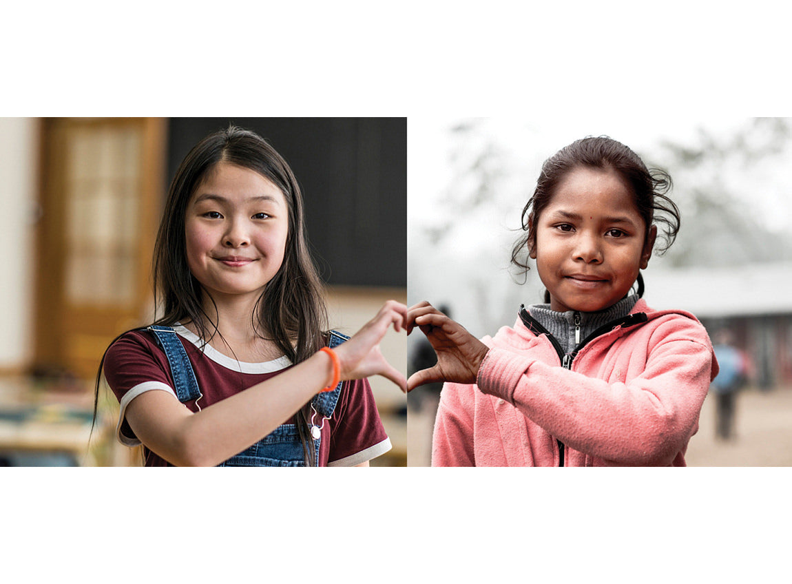 Two girls from different places and with different backgrounds form a heart with their fingers.