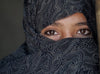 A close-up of a girl wearing a black headscarf showing only her eyes.
