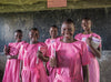Five girls wearing pink uniforms stand in front of a chalkboard, each carrying a book in their arms.