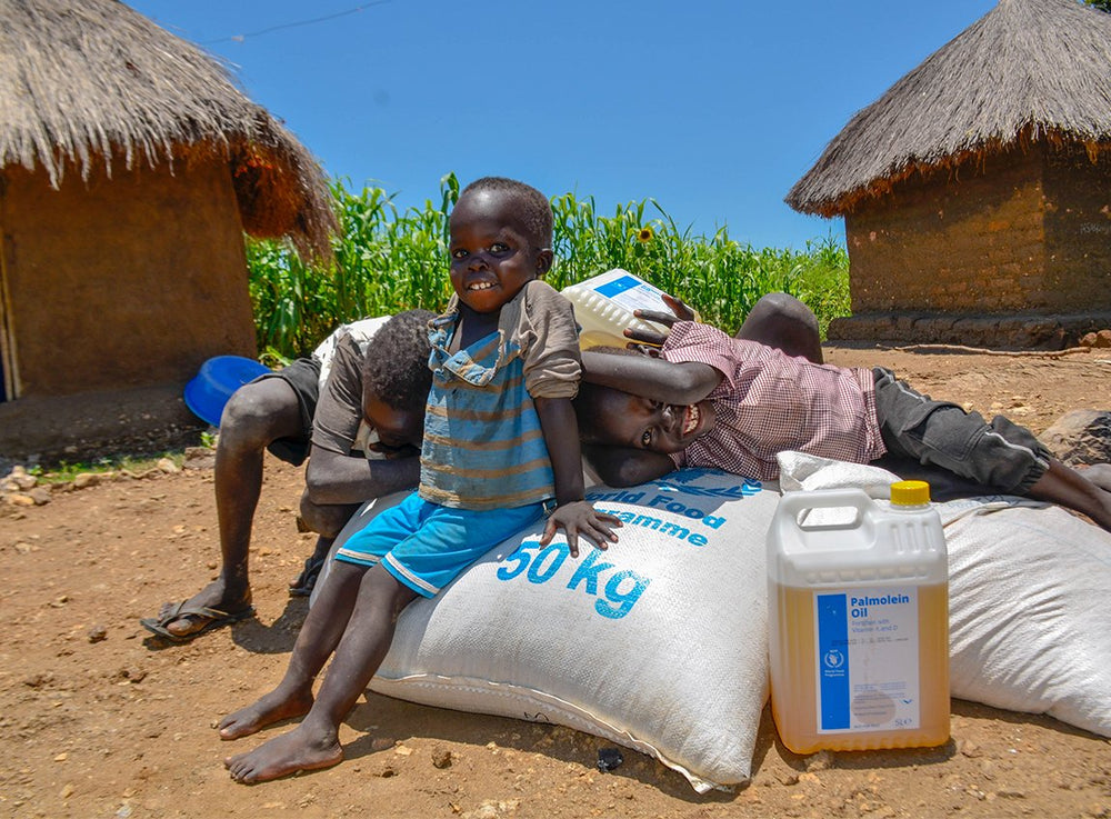 Several young boys smile as they sit or lie atop bags of food and a nearby jug of cooking oil.
