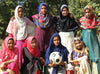 Eight young girls in saris pose for the camera. A girl in the middle holds a large soccer ball in her hands.