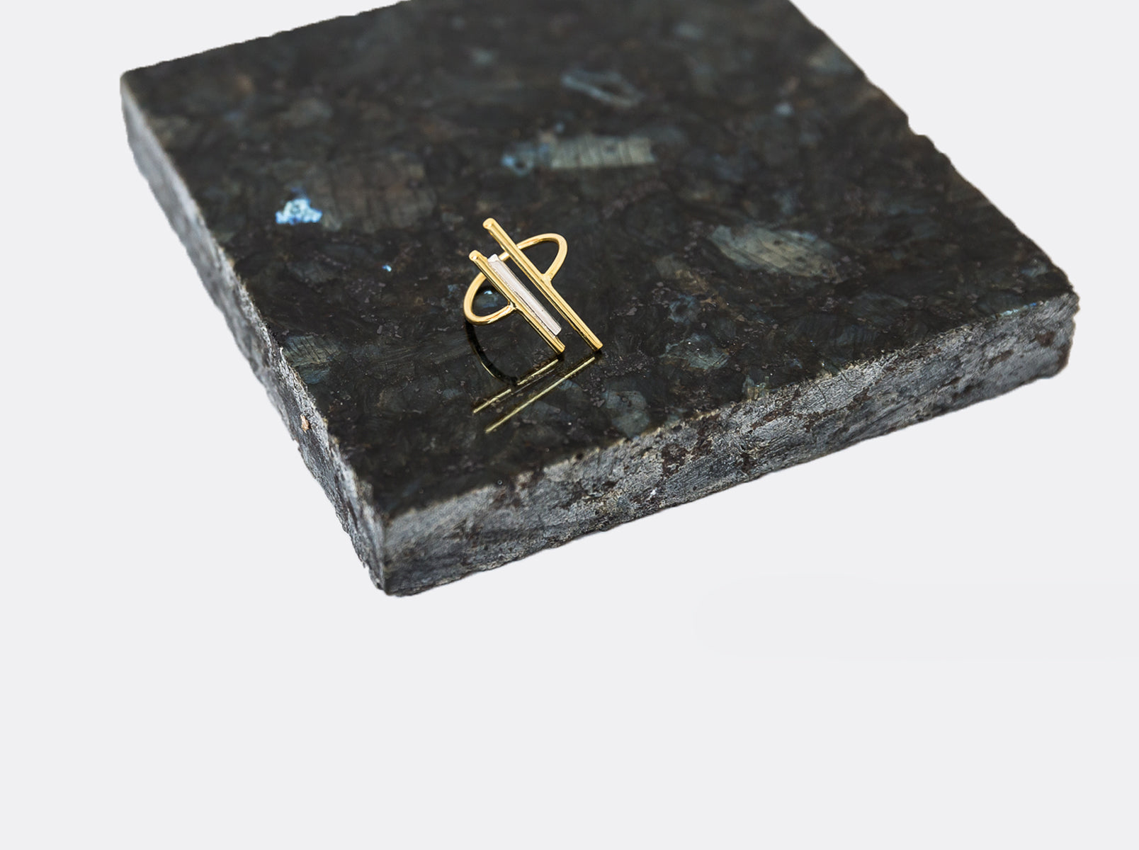 A two toned gold and silver ring sits on a granite platform.