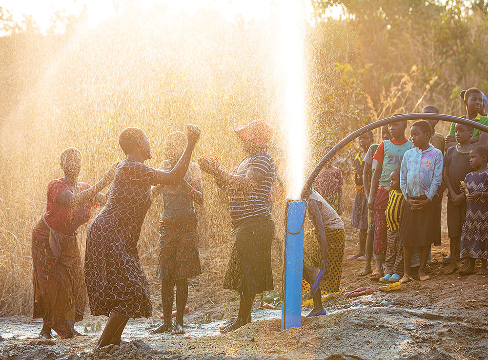 A group of people cheer as a new water pump sprays water.